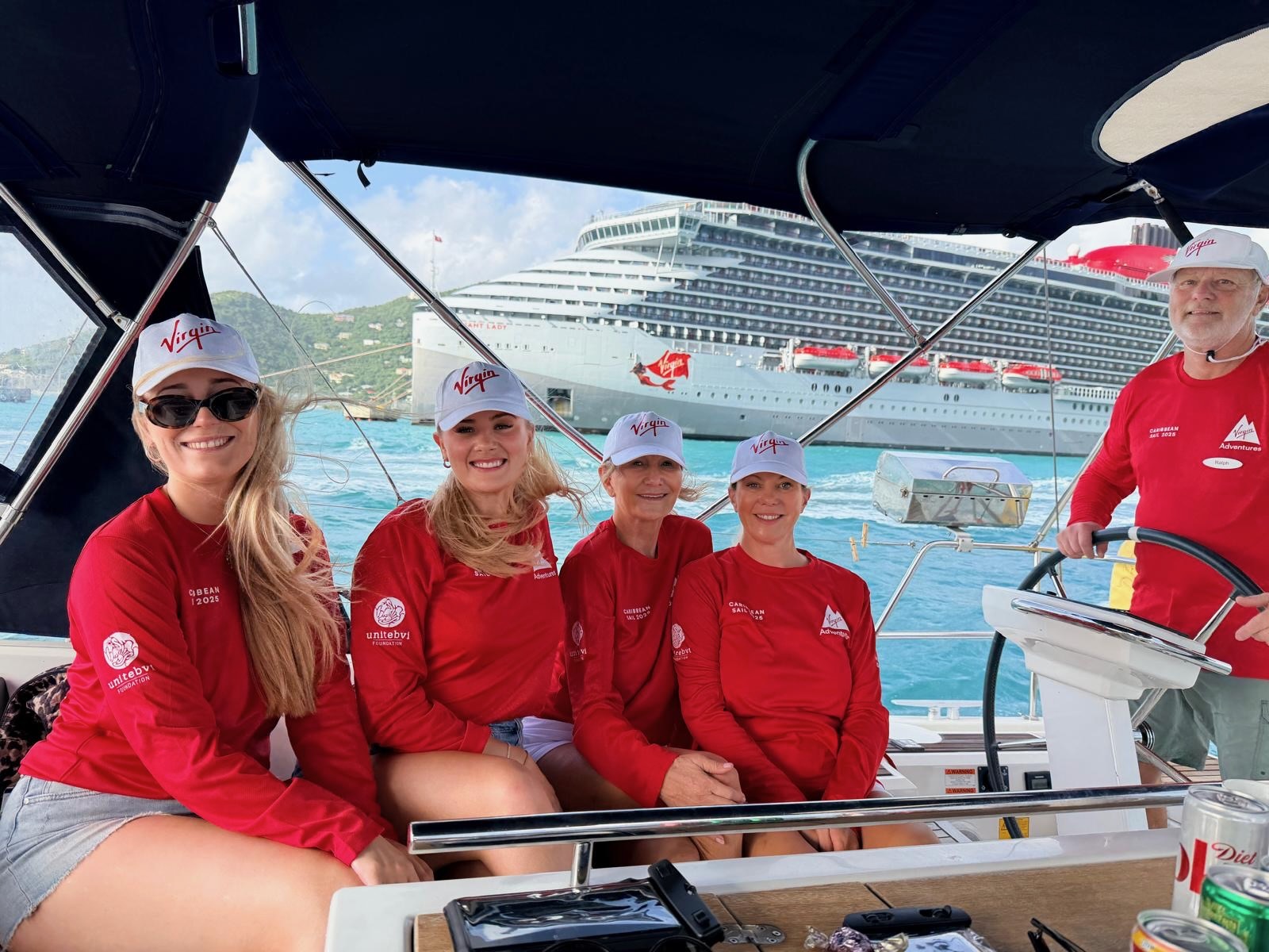A group of female sailors on a monohull yacht in the British Virgin Islands, passing Virgin Voyages Valiant Lady