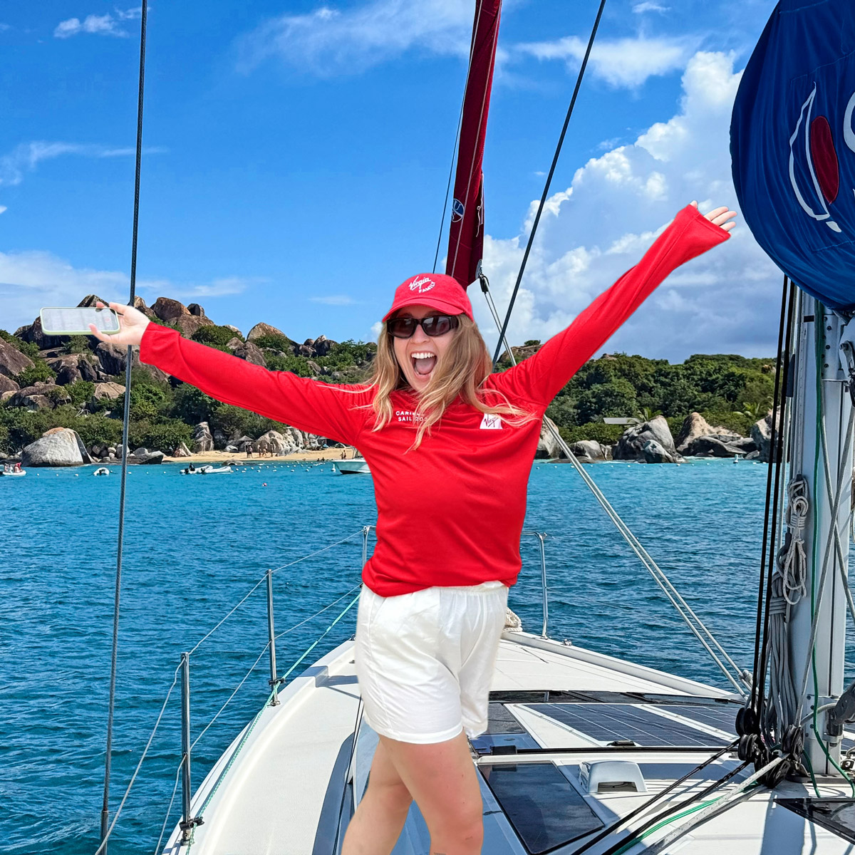 Joyous Virgin Adventures crew member, wearing red, arms outstretched on board a yacht near The Baths, Virgin Gorda, British Virgin Islands.