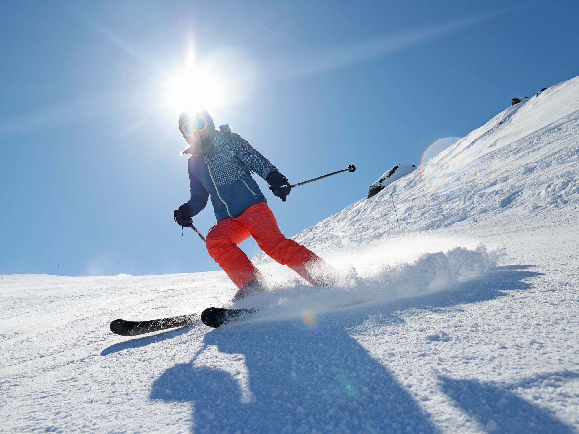 Looking up a skier, wearing red ski trousers, coming down a ski slope on a sunny winter day in France