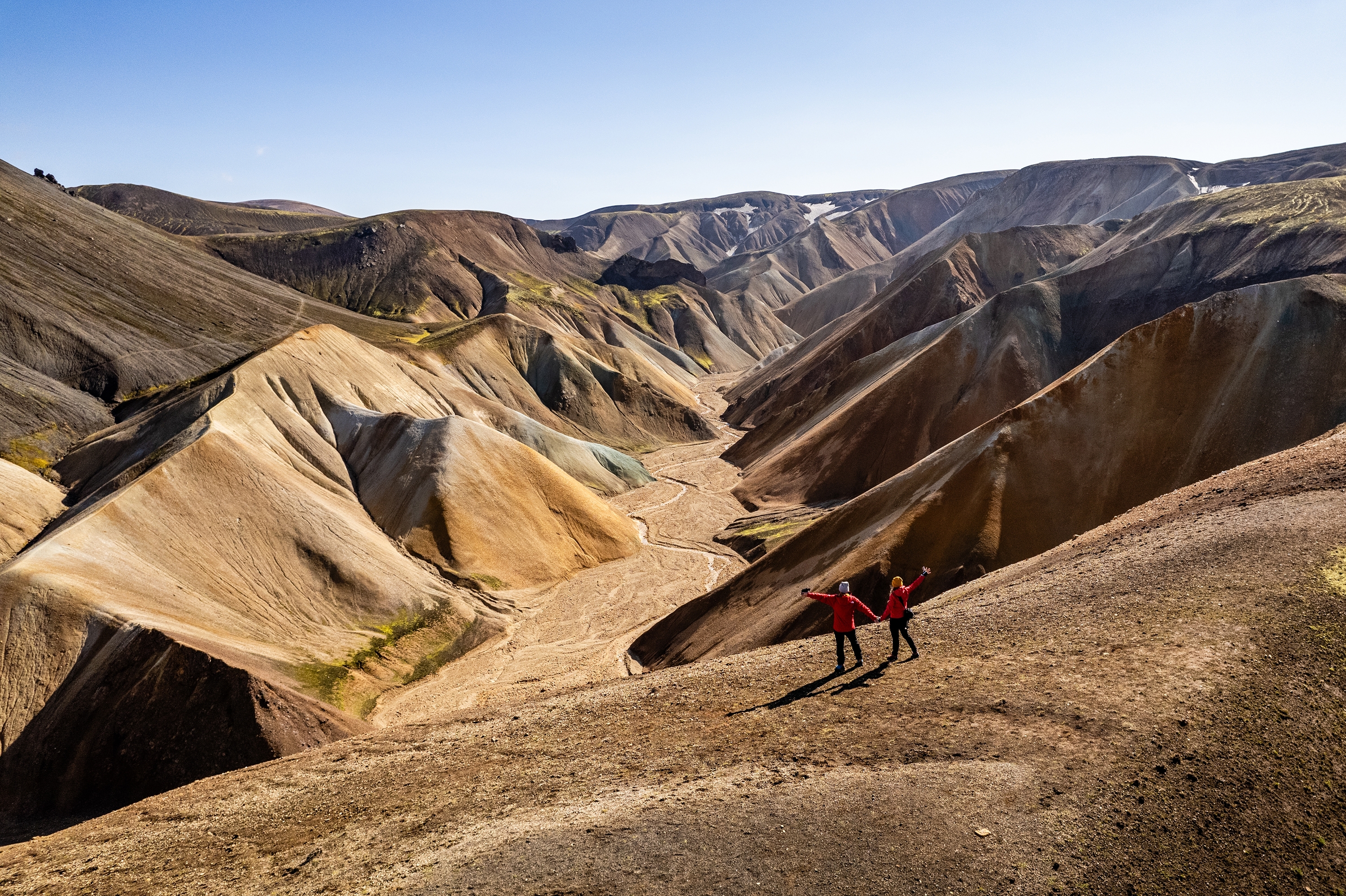 Couple hiking in stunning, rugged, and colorful mountainous Landmannalaugar terrain in Iceland showcasing geological formations with a vibrant sky